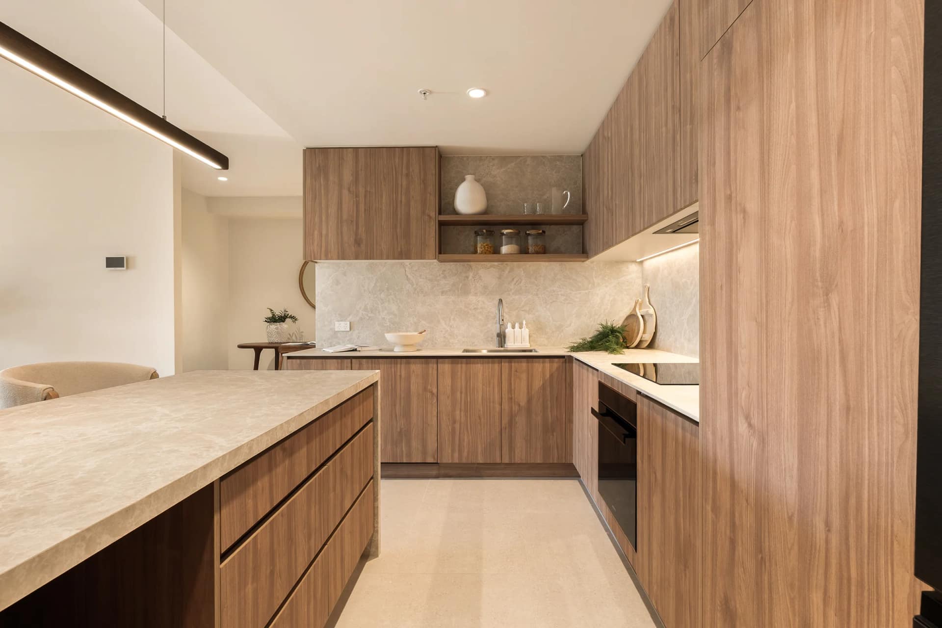 The completed kitchen: full-height timber-toned joinery, stone splashback and integrated oven, the Lusso Stone island bench in the foreground