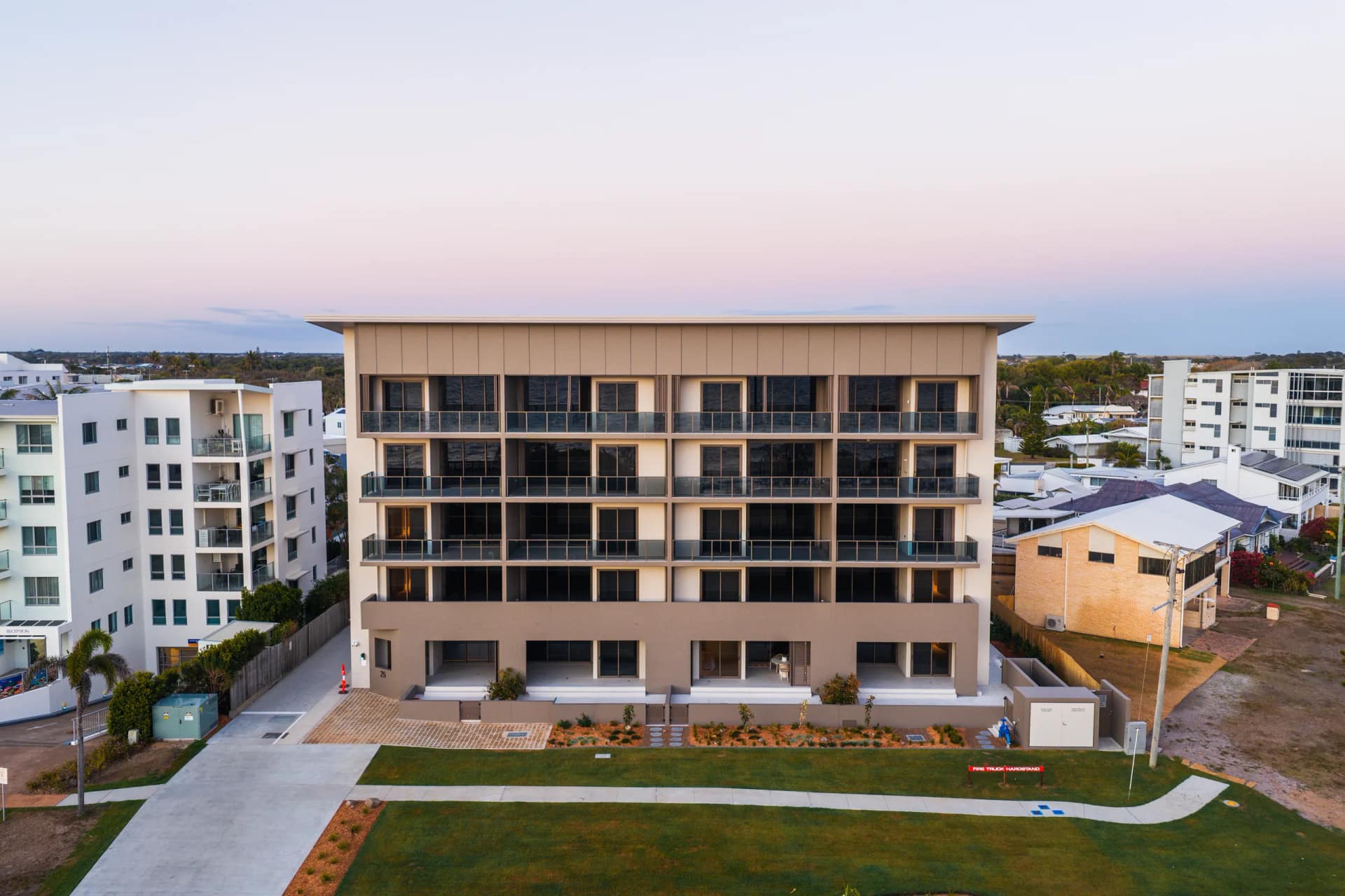 The completed residence at dusk, photographed from above the Esplanade — four levels of balconies under the deep roof, the new landscaping and lawn below