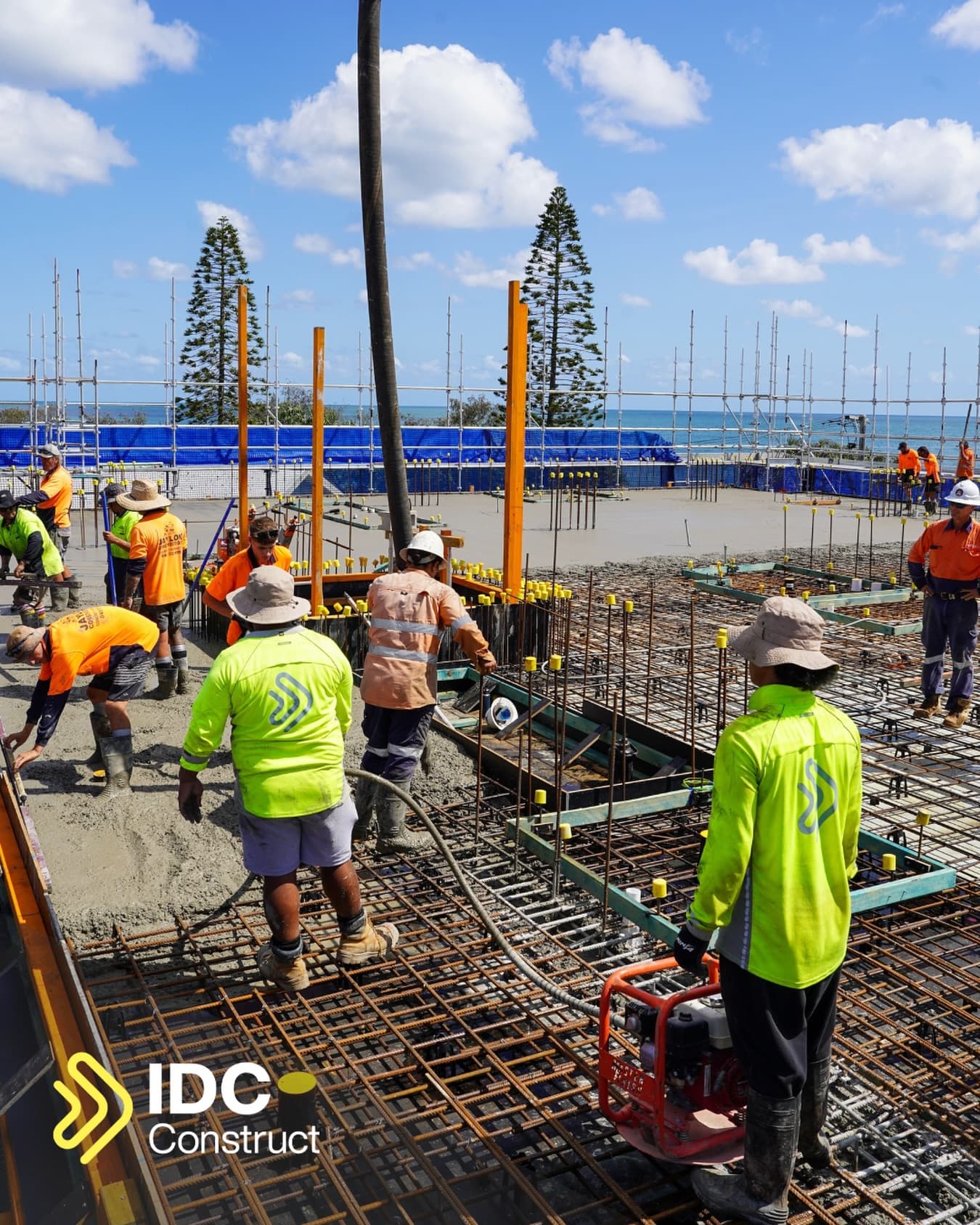 Concrete crews working a slab pour on the Mira Living site, with a concrete boom line overhead, scaffolding and the Coral Sea behind