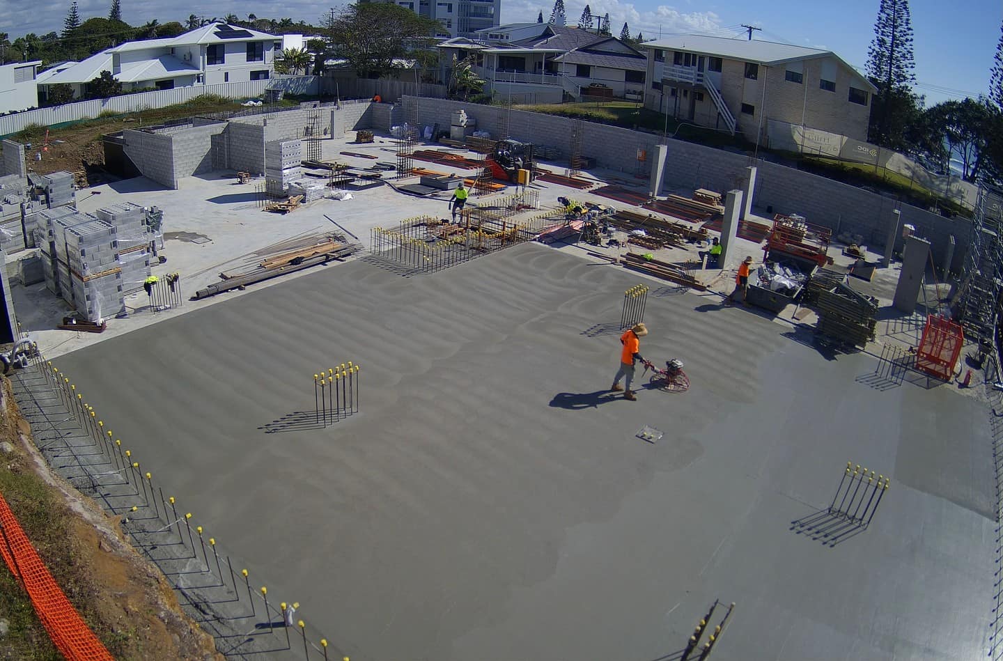 Completed basement slab ringed by blockwork walls as a worker power-trowels the fresh concrete